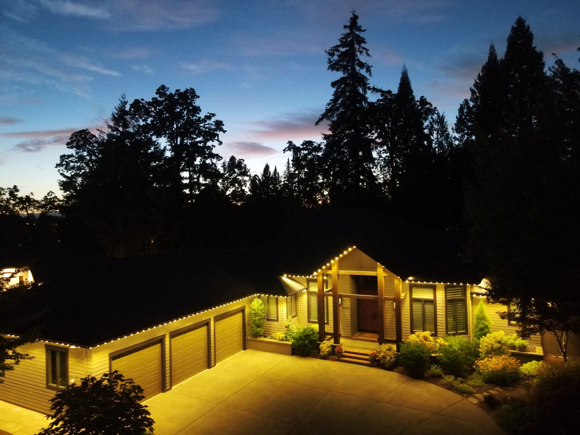 Aerial drone shot at dusk of a Salem home with warm white permanent LED roofline lighting installed by Timber Glow Lights