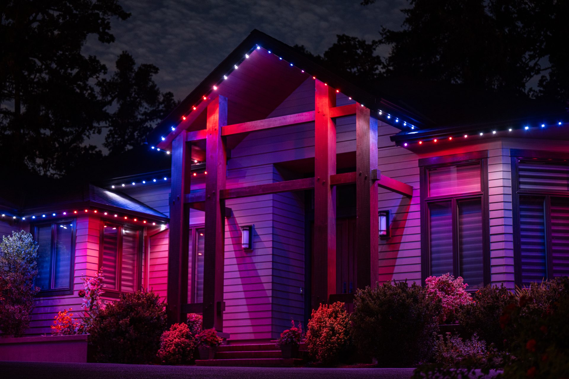 Home with wooden beam entryway lit in patriotic red, white, and blue permanent LED lights
